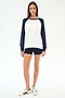 A woman faces forward on a plain white background wearing the SPLITS59 Andie Oversized Colorblock Fleece in Indigo/White, paired with navy modal spandex shorts and white Adidas sneakers.