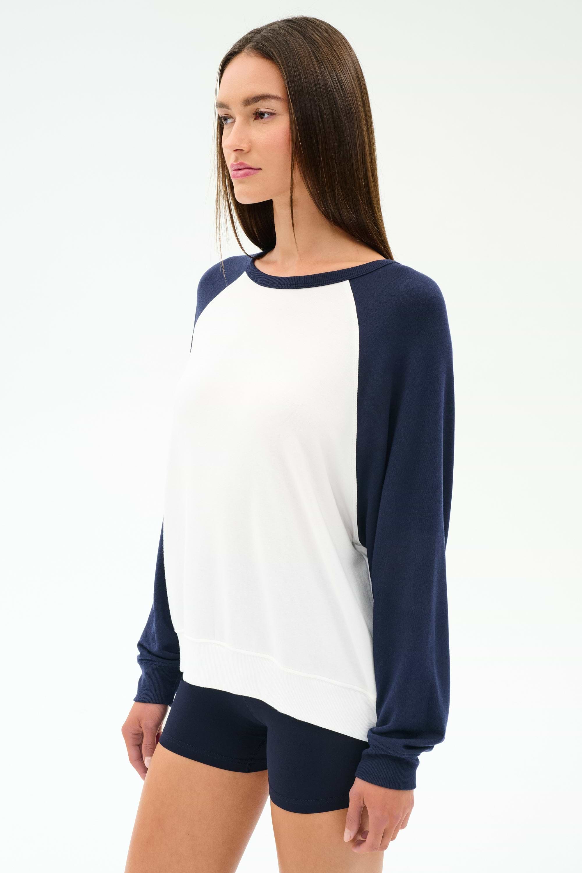 A woman wears the SPLITS59 Andie Oversized Colorblock Fleece in Indigo/White, paired with navy shorts, standing against a plain light background.