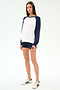 A woman stands against a white background wearing the SPLITS59 Andie Oversized Colorblock Fleece in Indigo/White, navy shorts, and white sneakers with navy stripes.