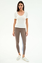 A woman faces forward wearing the SPLITS59 Ashby Rib Short Sleeve in white, taupe spandex-blend leggings with a blue stripe, and silver sneakers against a plain white background.