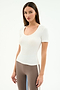 A woman with straight brown hair wears the SPLITS59 Ashby Rib Short Sleeve in white and taupe spandex blend leggings with a white side stripe, standing against a plain white background.