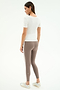 A woman stands against a white background, wearing the SPLITS59 Ashby Rib Short Sleeve in white and taupe leggings with a white side stripe, both in a comfy spandex blend, paired with white sneakers. She is turned slightly to the side.