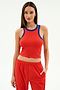 A woman stands against a plain background wearing the SPLITS59 Kiki Rib Crop Tank in Lotus Red/Cobalt with soft baby rib fabric and matching red pants, one hand in her pocket.