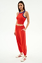 A woman wears the SPLITS59 Kiki Rib Crop Tank in Lotus Red/Cobalt, paired with red track pants with a white stripe and white sneakers with red accents—an ideal outfit for gym sessions.