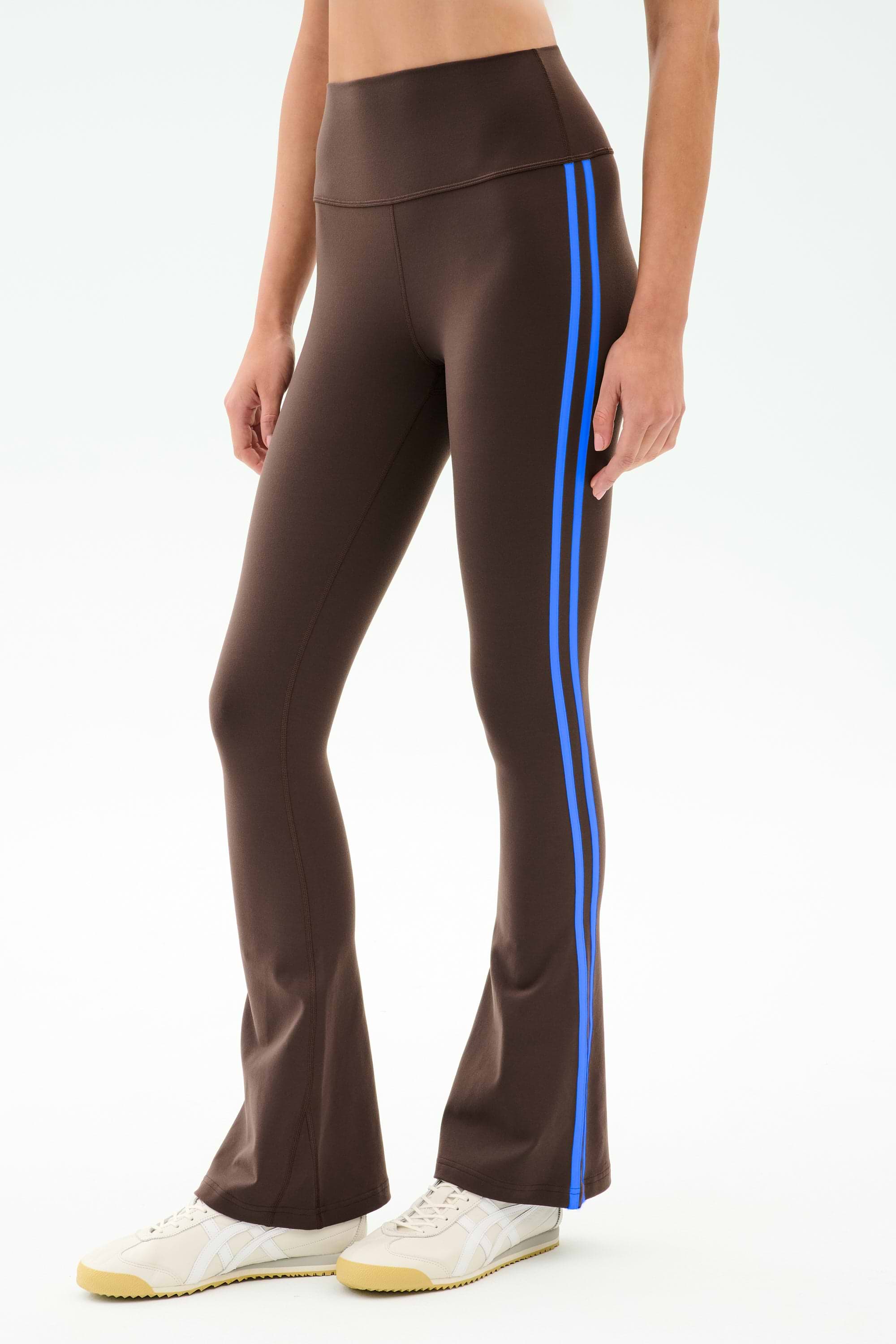 Model wears the SPLITS59 Raquel High Waist Supplex Flare in Dark Chocolate/Classic Blue, featuring blue side stripes and a comfy 4-way stretch fabric—ideal for gym workouts—paired with white sneakers against a plain backdrop.