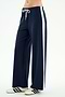A person stands against a plain light background wearing the SPLITS59 Willow Airweight Wide Leg pants in Indigo/White—navy blue pants with a white side stripe made from stretch activewear fabric—and white sneakers with navy stripes.