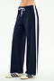 A person stands against a plain light background wearing the SPLITS59 Willow Airweight Wide Leg pants in Indigo/White—navy blue pants with a white side stripe made from stretch activewear fabric—and white sneakers with navy stripes.