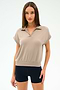 A woman poses against a plain background wearing the SPLITS59 Evie Fleece Sleeveless Polo in Latte and black fitted stretch shorts.