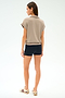 A woman stands facing away, wearing the SPLITS59 Evie Fleece Sleeveless Polo in Latte, black shorts, and beige sneakers with burgundy stripes against a plain white background.