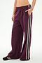 Wearing SPLITS59 Dallas French Terry Wide Leg Sweatpant in Dark Cherry/Black—a loose-fitting, 100% cotton design with white and black side stripes—this person also has a matching top partially visible and black shoes, standing against a plain white background.