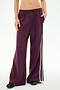 A person wearing SPLITS59’s Dallas French Terry Wide Leg Sweatpant in Dark Cherry/Black—loose-fitting 100% cotton sweatpants featuring black and white side stripes—stands with one hand in a pocket.