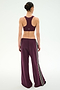 A person stands with their back to the camera, wearing SPLITS59’s Dallas French Terry Wide Leg Sweatpant in Dark Cherry/Black—crafted from 100% cotton and featuring side stripes—paired with a matching maroon sports bra, set against a plain white background.
