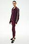 A person stands in a studio against a plain white background, wearing the SPLITS59 Goldie French Terry Oversized Half Zip in Dark Cherry/Black—an oversized zip-up jacket with striped sleeves crafted from soft cotton fabric—paired with matching maroon leggings and black sneakers.