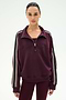 A woman wearing the SPLITS59 Goldie French Terry Oversized Half Zip in Dark Cherry/Black, crafted from soft cotton-blend fabric with white striped sleeves, paired with matching maroon leggings, stands against a plain light background.