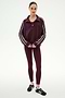 A woman stands facing forward against a white background, wearing the SPLITS59 Goldie French Terry Oversized Half Zip in Dark Cherry/Black and matching maroon leggings, paired with black sneakers.