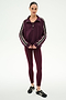 A woman stands facing forward against a white background, wearing the SPLITS59 Goldie French Terry Oversized Half Zip in Dark Cherry/Black and matching maroon leggings, paired with black sneakers.