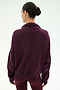 A woman with dark hair in a bun stands with her back to the camera against a plain light background, wearing the SPLITS59 Goldie French Terry Oversized Half Zip in Dark Cherry/Black.