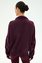 A woman with dark hair in a bun stands with her back to the camera against a plain light background, wearing the SPLITS59 Goldie French Terry Oversized Half Zip in Dark Cherry/Black.
