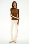 A person faces forward wearing the SPLITS59 Isabelle Airweight Lite Mock Neck - Toffee/Creme, cream flared spandex pants with side stripes, and white sneakers.