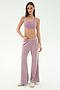 A woman stands in a studio wearing the SPLITS59 Joy Velour Pant in Blush, a mauve sports bra, and white sneakers against a plain white background.