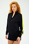 A curly-haired individual wears the SPLITS59 Max Rigor Track Jacket in Black/Chartreuse with a chic black dress, set against a simple backdrop.