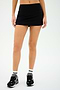 A person wearing the Sally Rigor Skort from SPLITS59, paired with black and white sneakers and white socks featuring black stripes, stands against a plain background.