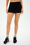 A person wearing the Sally Rigor Skort from SPLITS59, paired with black and white sneakers and white socks featuring black stripes, stands against a plain background.