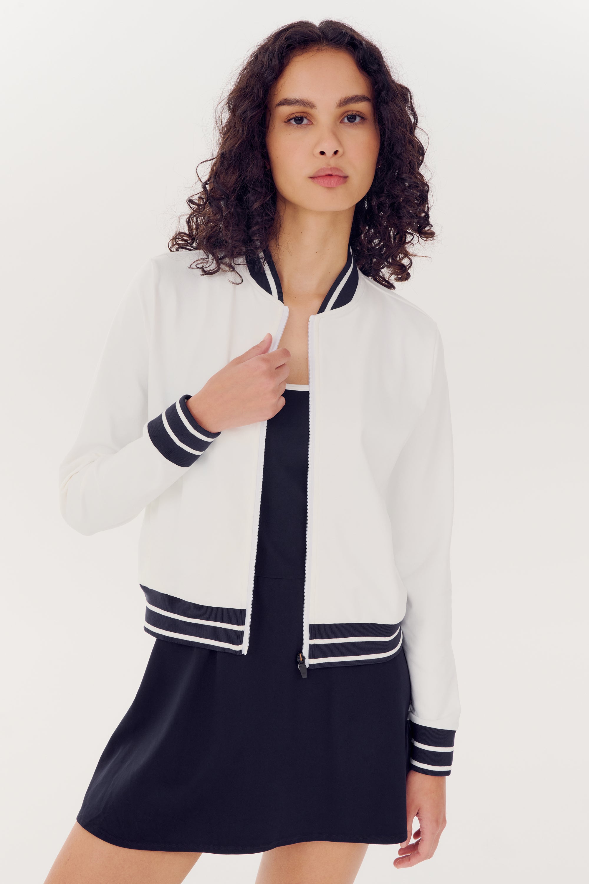 Young woman posing in a SPLITS59 Ever Supplex Jacket in white and a spandex black dress.