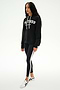 A woman wearing a black SPLITS59 Stella French Terry Oversized Hoodie with "Splits59 Los Angeles," black leggings with white stripes, and white sneakers stands against a white background.