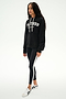 A woman wearing a black SPLITS59 Stella French Terry Oversized Hoodie with "Splits59 Los Angeles," black leggings with white stripes, and white sneakers stands against a white background.