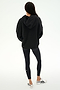 A person stands with their back to the camera, wearing the SPLITS59 Stella French Terry Oversized Hoodie in black, paired with black leggings featuring a white stripe and white sneakers, set against a plain white background.