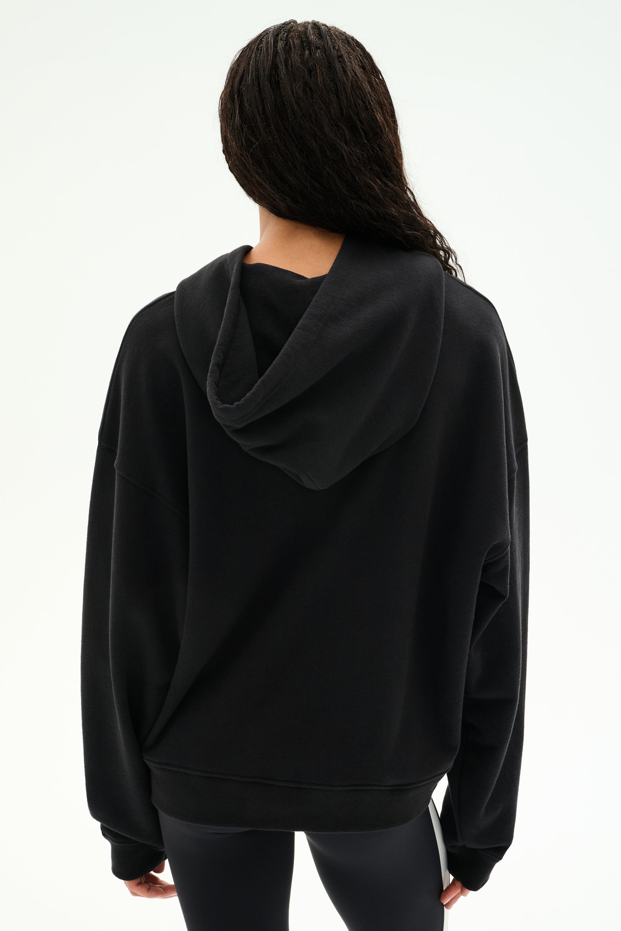 A person stands with their back to the camera against a plain light background, wearing the SPLITS59 Stella French Terry Oversized Hoodie in black and black leggings.