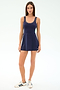 A woman faces forward wearing the SPLITS59 Martina Rigor Color Block Dress in Indigo/Spearmint, made from stretch nylon-spandex, paired with white sneakers featuring navy stripes, against a plain light background.