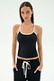 A woman stands facing forward in the SPLITS59 Airweight Tank - Black/White, paired with black pants with a white drawstring—an ideal Pilates outfit—hands in pockets, set against a plain light background.