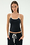 A woman stands facing forward in the SPLITS59 Airweight Tank - Black/White, paired with black pants with a white drawstring—an ideal Pilates outfit—hands in pockets, set against a plain light background.