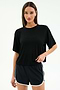 A woman stands against a plain background wearing the SPLITS59 Djuna Oversized Jersey Tee in black and black athletic shorts with white trim, perfect for gym workouts.
