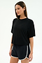 A woman wears the SPLITS59 Djuna Oversized Jersey Tee in black, paired with black athletic shorts with white trim, standing against a plain light background.