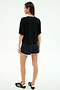 A woman faces away, wearing a loose black tee and SPLITS59 Megan Woven Nylon Run Shorts in Black/Creme, paired with black sneakers with white accents, all set against a plain light background.