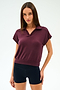 A woman faces forward, wearing the SPLITS59 Evie Fleece Sleeveless Polo in Dark Cherry and black shorts against a plain white background.