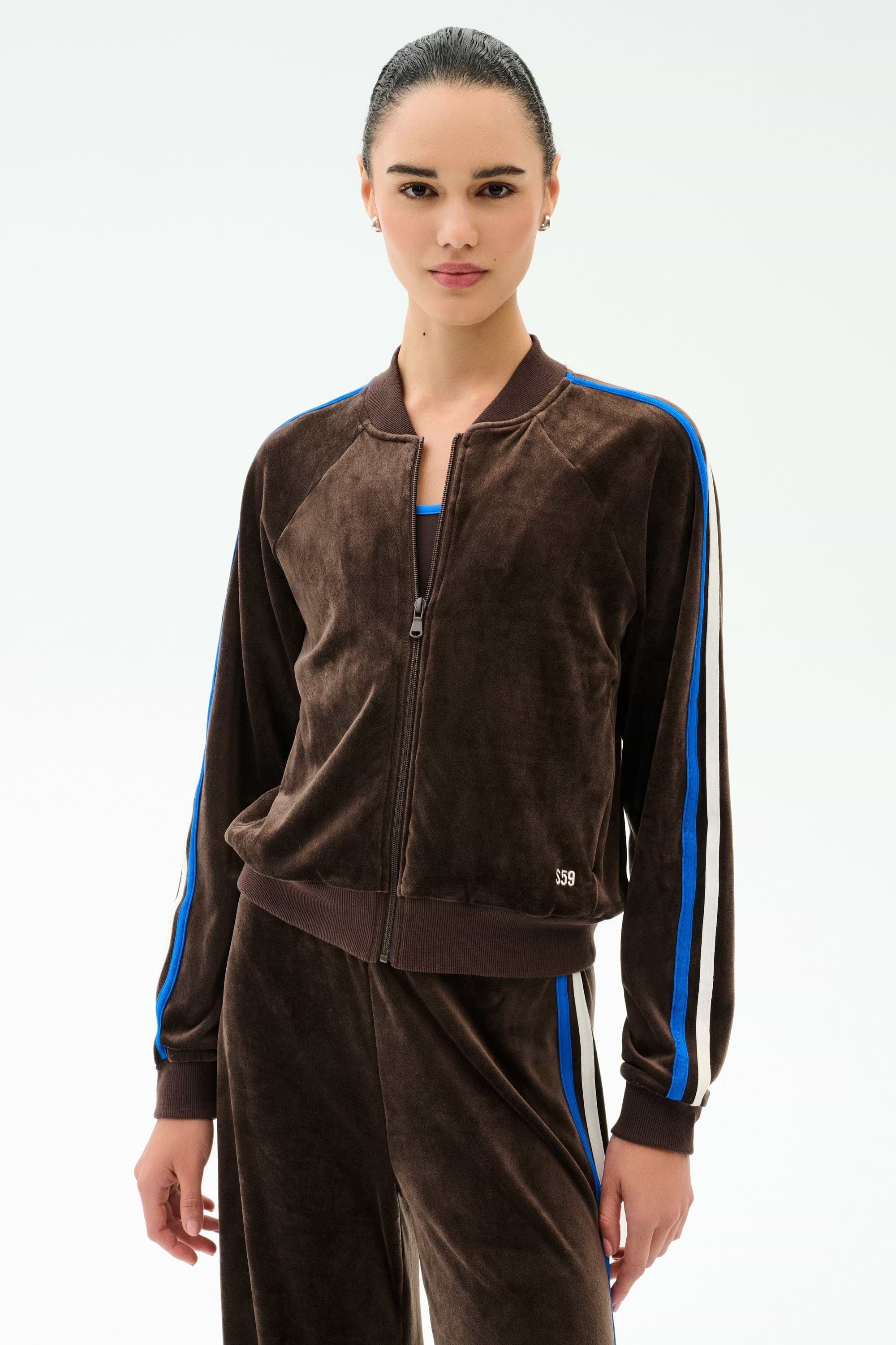 Warming up in the SPLITS59 Heritage Velour Bomber in Dark Chocolate/Classic Blue, she stands against a plain light background, pairing it with matching Heritage Velour Pants for effortless style.