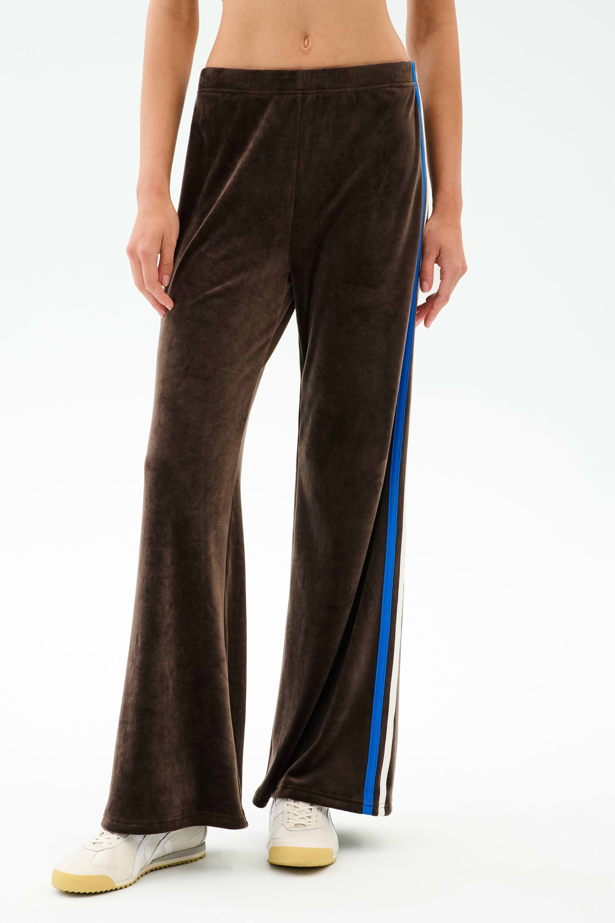 Model wearing the SPLITS59 Heritage Velour Pant in Dark Chocolate/Classic Blue, featuring ankle-length wide legs and blue and white side stripes, paired with white sneakers against a plain background.