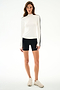 A woman wears the SPLITS59 Isabelle Airweight Lite Mock Neck - White/Black with black spandex shorts and beige sneakers against a plain white background.