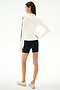 Woman wearing the SPLITS59 Isabelle Airweight Lite Mock Neck - White/Black, paired with black shorts and white sneakers, stands with her back to the camera against a plain background.