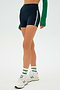 Wearing a green long-sleeve top, SPLITS59 Ella Airweight High Waist Short in Indigo/White, white socks, and white sneakers.
