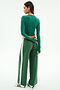 A woman stands facing away in the SPLITS59 Louise Rib Long Sleeve Crop in arugula and matching green wide-leg pants with a white stripe, paired with white sneakers featuring black stripes, set against a plain background.