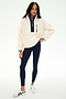 A person stands against a plain white background wearing the SPLITS59 Reese Sherpa Half Zip Pullover in Creme/Indigo, made from 100% polyester, paired with navy leggings and white sneakers.