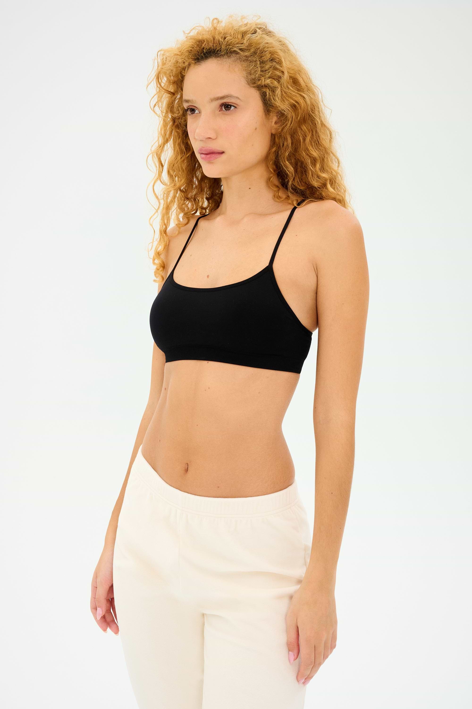A person with long curly hair, confidently wearing the Splits59 Loren Seamless Bra in black and white pants, stands against a plain background.