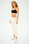 A person with curly hair exudes confidence in a black Loren Seamless Bra by Splits59, beige pants, and white sneakers. They stand against a plain white background, exemplifying effortless style and comfort that's ideal for gym workouts.