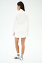 A woman stands facing away against a plain white background, wearing the SPLITS59 Kaia Active Rib Skort in White, paired with a matching long-sleeve white top, white socks, and white sneakers with black accents.