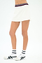A model wears the SPLITS59 Kaia Active Rib Skort in White, featuring a striped waistband, paired with white socks and sneakers—ideal for court sports or gym workouts—standing against a plain white background.